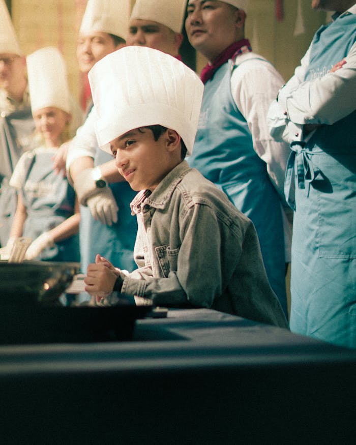 services-01 A young boy in a chef hat participates in a lively cooking class with instructors.