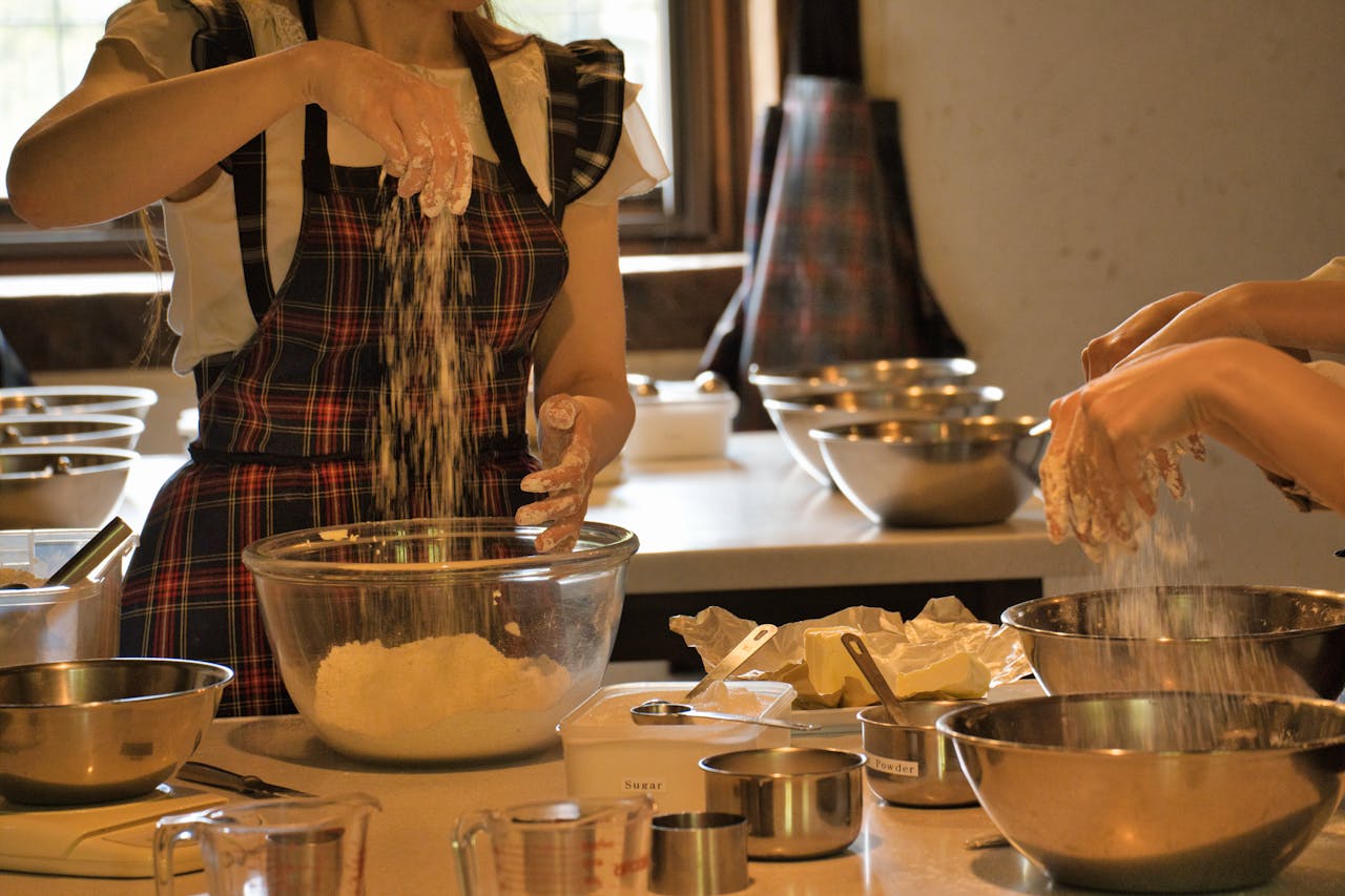 services-02 A woman in an apron mixes flour in a kitchen setting, showcasing hands-on cooking.